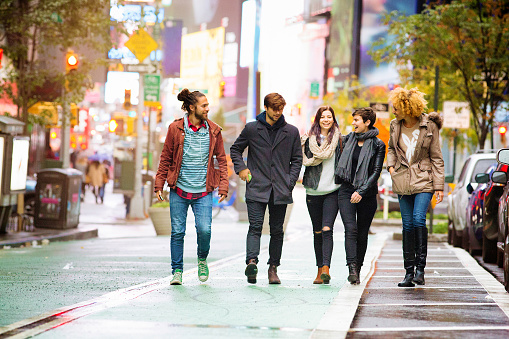 Five friends walking happy in Times square, Manhattan, on a rainy Autumn day.  They are dressed in warm Fall clothing.