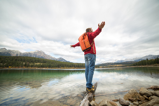 Man walking on a tree log on the lake. Focus on the foreground, mountains on the background.