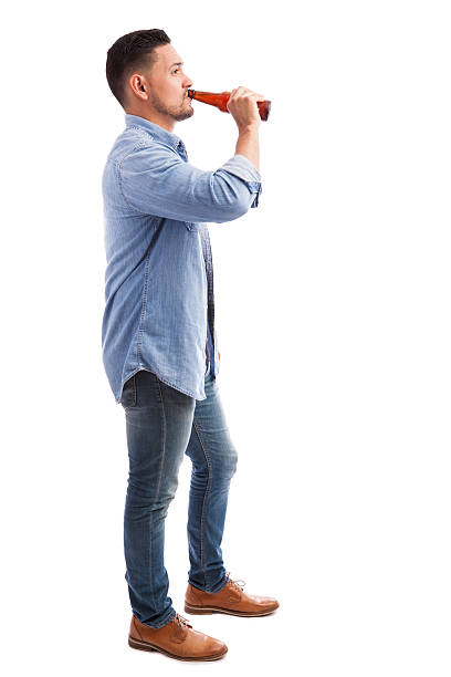 Hispanic man drinking beer Full length profile view of a young Hispanic man drinking beer from a bottle against a white background drinking beer stock pictures, royalty-free photos & images