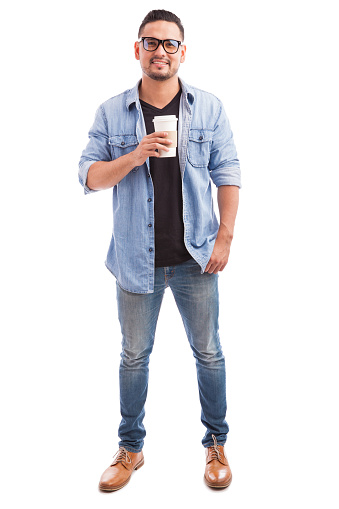 Portrait of a young hipster man wearing glasses and drinking coffee from a cup in a white background