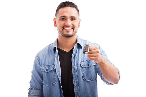 Portrait of a young happy man holding the keys for his brand new car in a white background