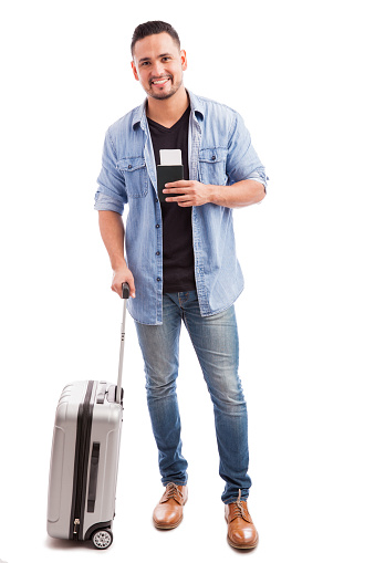 Full length portrait of a good looking guy carrying a suitcase and his passport before going on vacation