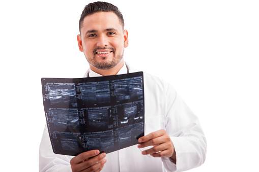 Young Hispanic radiographer examining some x-rays and smiling against a white background
