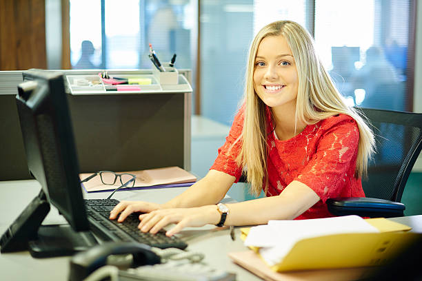 young female work placement office worker young female office worker or work experience student , sitting at her desk and looking at camera. school receptionist stock pictures, royalty-free photos & images