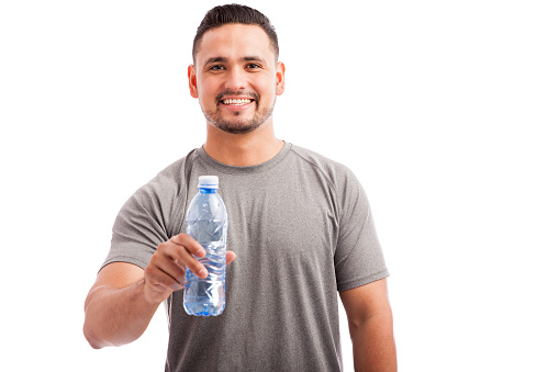 Portrait of a young man in sporty outfit offering a bottle of water to the camera and smiling