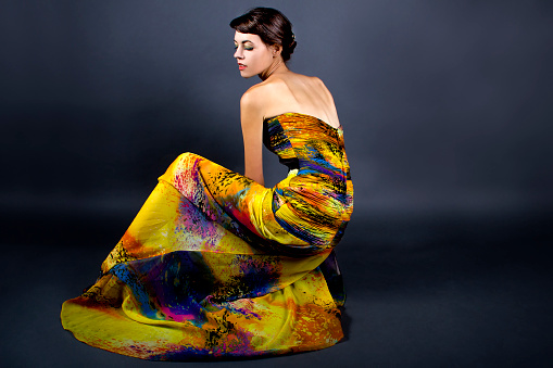 Woman modeling a yellow dress on a dark background for contrast.  She is wearing garment with a generic tie dye design.  The image is depicting the fashion industry and style.  The model is a caucasian female.