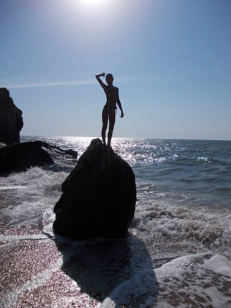 Beautiful girl on big stone in the sea stock photo