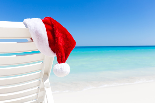 Santa Claus Hat on sunbed near  sandy beach with turquoise caribbean sea water. Tropical Christmas Card