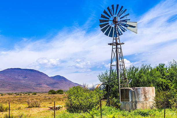 Windmill water pump in the Karoo with the water reservoir and green flora. A traditional sight seen in the South African countryside.