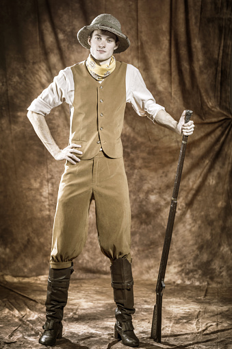 Attractive young man in period costume safari hunter standing with a hunting rifle. Sepia toned