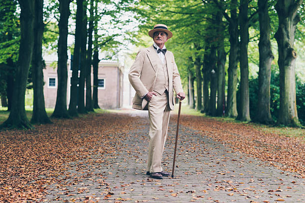 Wealthy senior retro dandy in suit standing with cane in avenue.