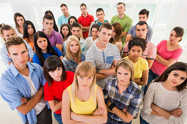 High angle view of large group of serious young people standing together with their arms crossed and looking at camera.