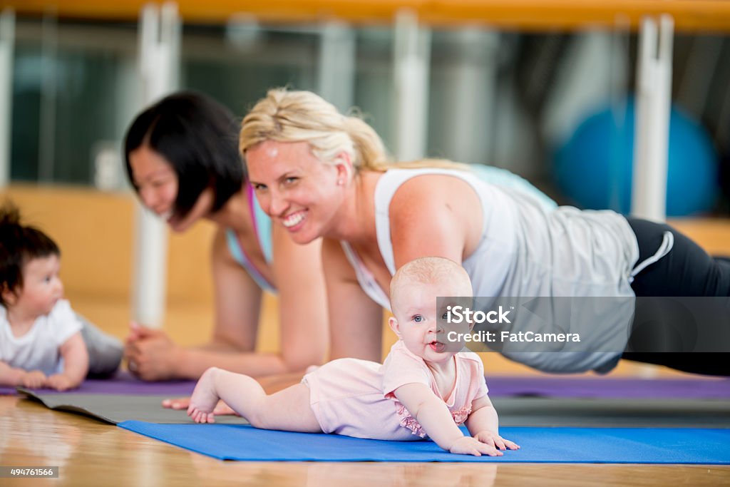 Mothers Exercising with Their Babies A multi-ethnic group of mother are in an exercise class at the gym while their babies play on the mats next to them. 12-17 Months Stock Photo