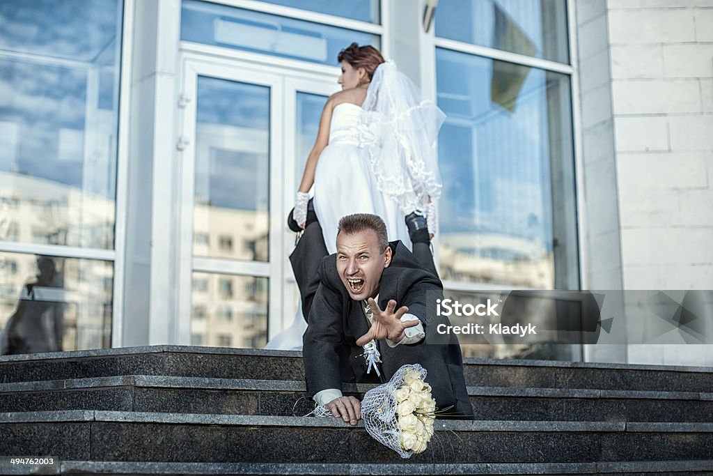 Bride makes groom to marry. Bride groom grabbed his leg and pulls the wedding. Escaping Stock Photo