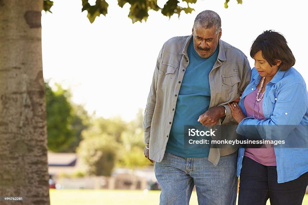 Senior Woman Helping Husband As They Walk In Park Together Senior Woman Helping Husband As They Walk In Park Together Holding His Arm Active Seniors Stock Photo