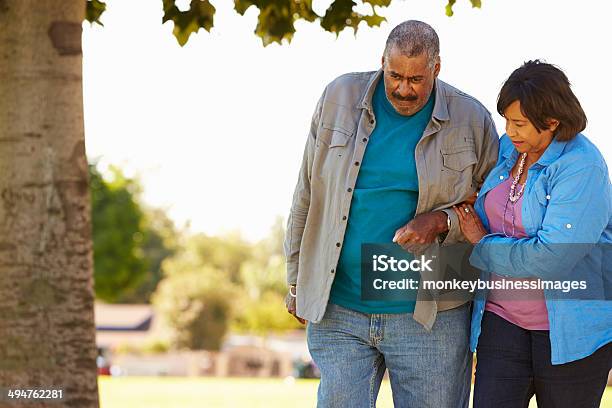 Senior Woman Helping Husband As They Walk In Park Together Stock Photo - Download Image Now