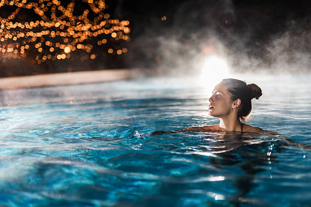 mujer joven disfrutando de una piscina climatizada en la noche. - hot spring fotografías e imágenes de stock