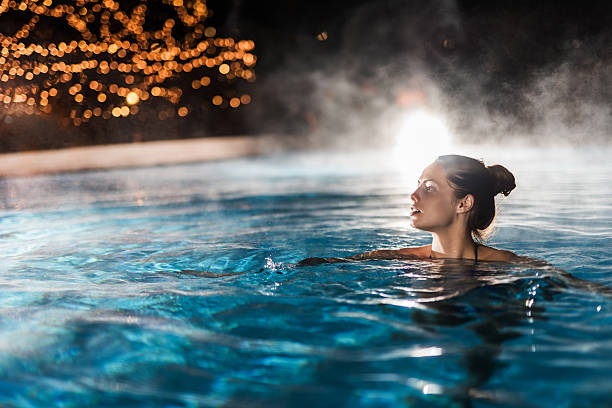 Young woman enjoying in a heated swimming pool at night. Beautiful woman swimming in a swimming pool with steam. hot spring stock pictures, royalty-free photos & images