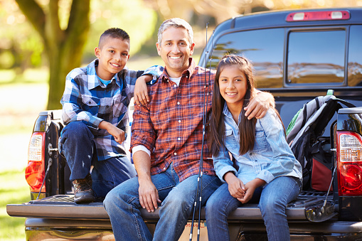 Father And Children Sitting In Truck On Camping Holiday Smiling To Camera