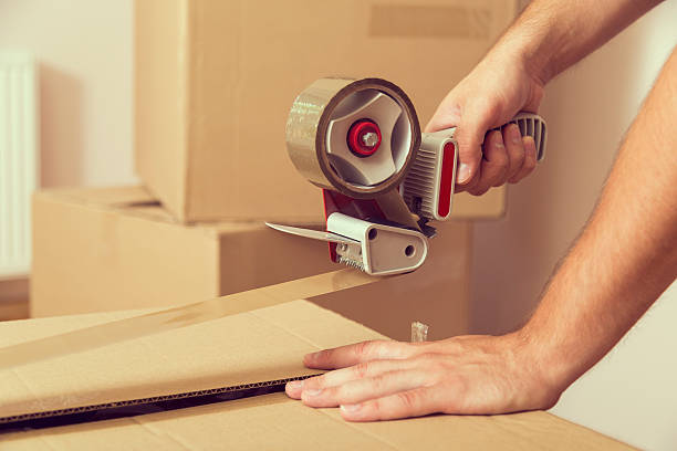 Packing Close up of a guy's hands holding packing machine and sealing cardboard boxes with duct tape packing stock pictures, royalty-free photos & images