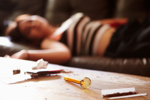 Woman Slumped On Sofa With Drug Paraphernalia In Foreground In House