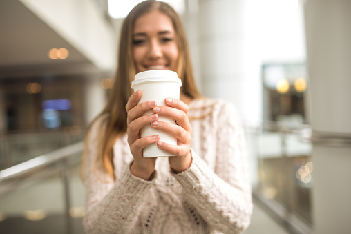 Young woman holding cup of coffee outdoors and smiling