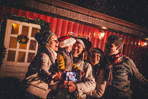 Family portrait on the first snow Cute multi-generation family in the backyard greeting the first snow for the winter season, and capturing the moment on the mobile phone  baby new years eve new years day new year stock pictures, royalty-free photos & images