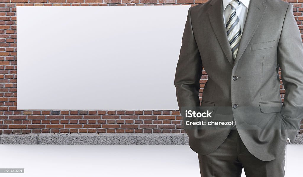 Businessman standing with hands in pockets Businessman standing with hands in pockets. Brick wall and white placard as backdrop Adult Stock Photo