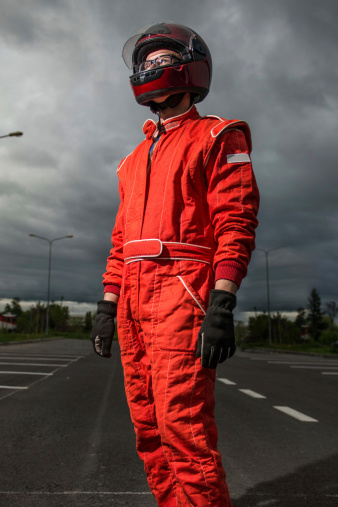 open-wheel single-seater racing car driver posing in dramatic sky background, outdoor, wearing protective helmet and red racing suit