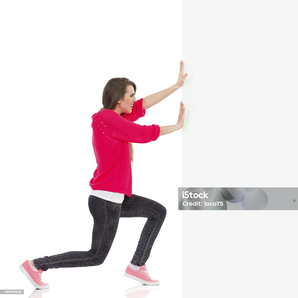 Young woman pushing the wall Young woman pushing the wall. Full length studio shot isolated on white. Pushing Stock Photo