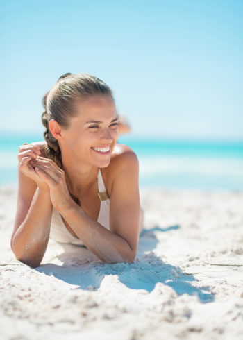 Portrait of smiling young woman laying on beach and looking into distance