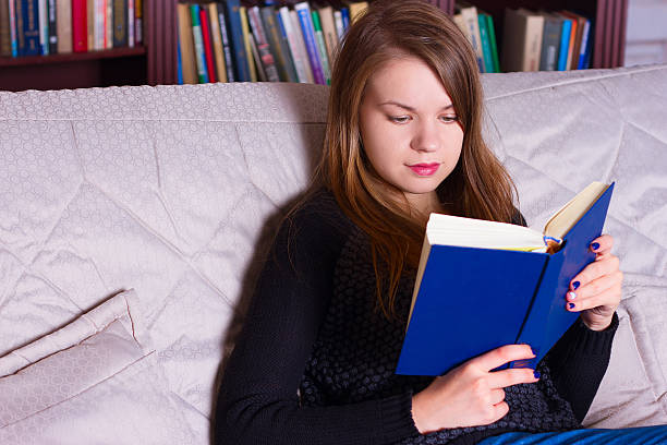 istock young woman sitting on sofa at home, reading a book 494808604
