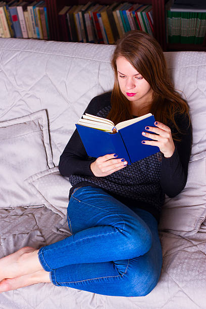 istock young woman sitting on sofa at home, reading a book 494808650