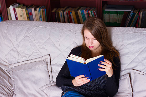 istock young woman sitting on sofa at home, reading a book 494808700