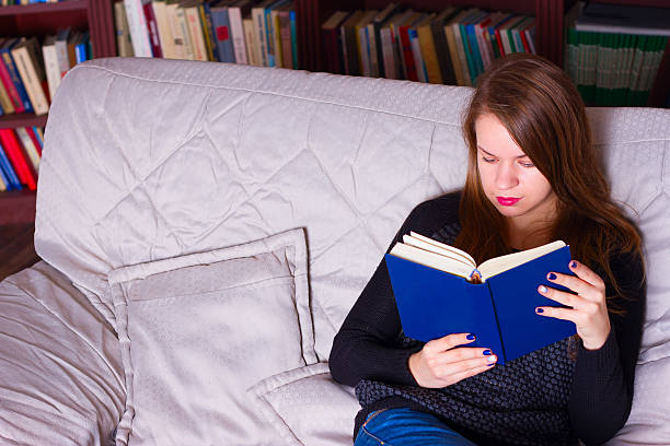 istock young woman sitting on sofa at home, reading a book 494808766
