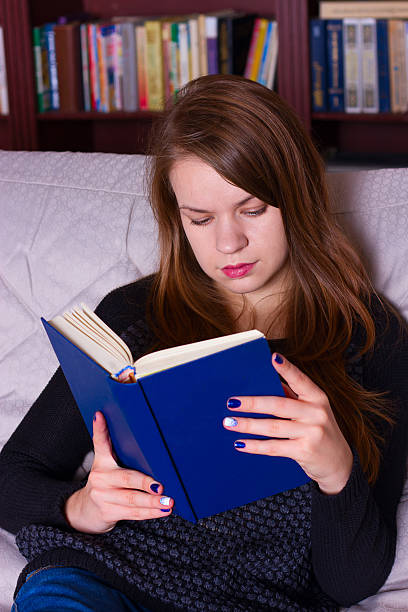 istock young woman sitting on sofa at home, reading a book 494809032