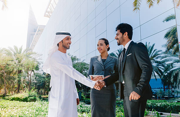 Arab business people shaking hands Two Middle Eastern businessman and business woman with traditional and suit clothes shaking hands on an agreement outside. persian gulf countries stock pictures, royalty-free photos & images