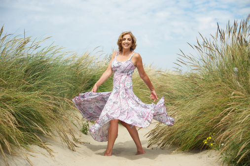 Portrait of a beautiful mature woman dancing in the sand at the beach