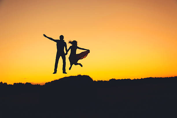 istock fun loving couple jumping at sunset, silhouette 494832010