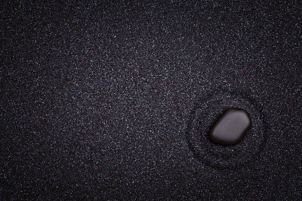 Black  zen stone with circle patterns in the sand A black  zen stone with circle patterns in the black grain sand black sand stock pictures, royalty-free photos & images
