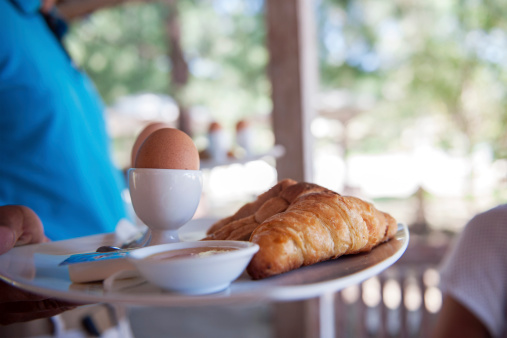 Waiter serving boiled eggs and croissant for breakfast