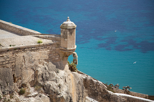 Watchtower of the Castilli de Santa Bárbara in Alicante, Valencia Region. In the background is the Turkish-blue Mediterranean Sea. 