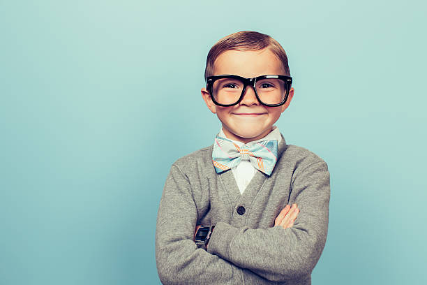 Young Boy Nerd with Big Smile A young boy dressed as a nerd with glasses is looking in the camera with a big smile on his face. He has a bow tie on and is in front of a blue wall. eccentric photos stock pictures, royalty-free photos & images