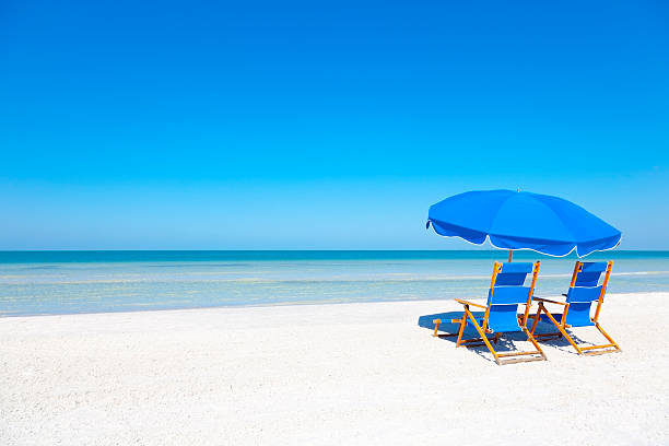 Lounge Chairs and Umbrella at the Beach Two blue beach loungers and umbrella at white sandy beach beach umbrella stock pictures, royalty-free photos & images