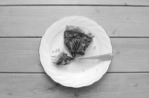 Half-eaten slice of pecan pie on a china plate with a dessert fork - monochrome processing