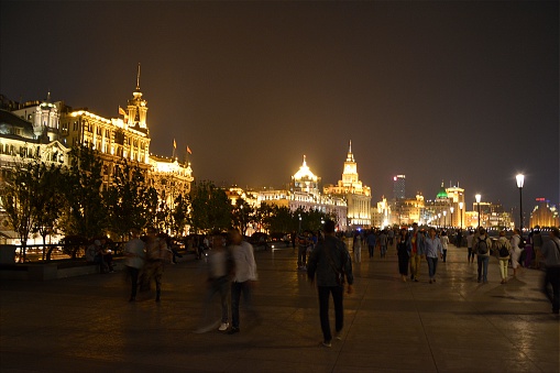 Shanghai, China - May 12, 2014: Crowd of tourists on the Bund at night, a scenic waterfront area in Shanghai. It is one of the most famous tourist destinations in Shanghai and houses buildings of various architectures. In the foreground, the lighten Shanghai Custom House building 