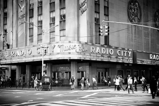 New York, United States - October 21, 2015: Pedestrians walk around and in front of Radio City Music Hall. The music hall is located in Madison Square Garden in New York City. This views shows a rickshaw driver and many pedestrians walking about. 