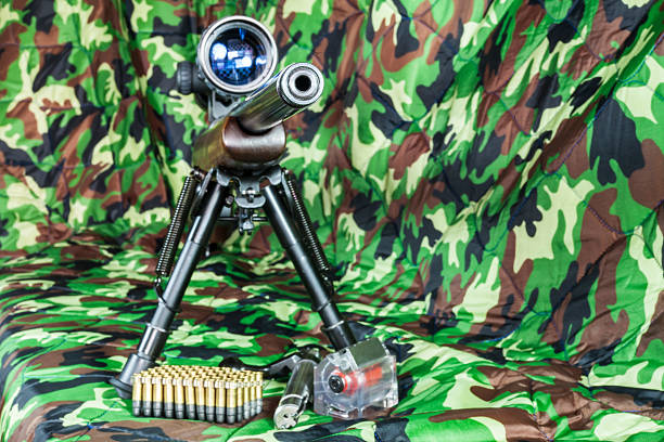 A marksman on burnt grass, is taking aim with his scope mounted on a precision cal .50 rifle.