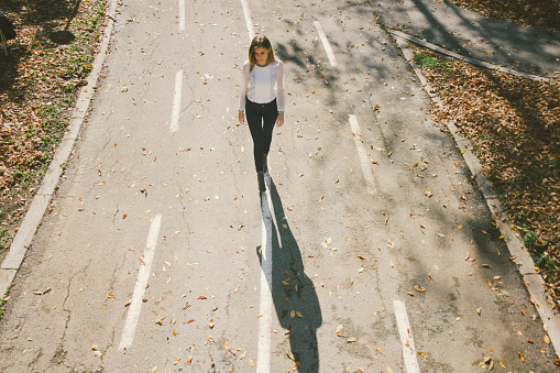 Cute brown hair girl walking down the street in autumn. Photo is taken with dslr camera and wide angle lens on sunny day. Kodak portra filter slightly applied in post processing.