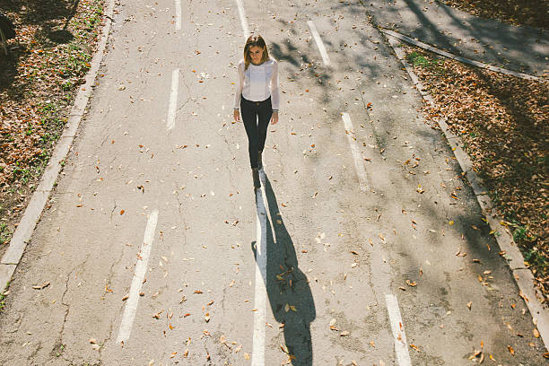 engraçado menina solitária a caminhar ao longo da rua no outono - single lane road imagens e fotografias de stock